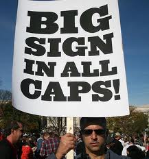 Man holds sign reading Big Sign In All Caps
